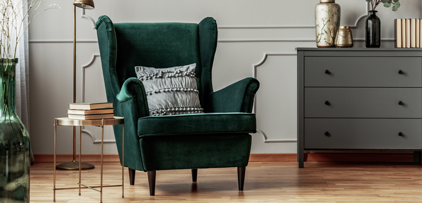 Fauteuil à oreilles vert en velours, table d'appoint, commode grise, livres et vases dorés, noirs et vert