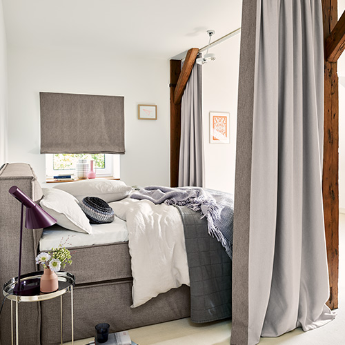 Chambre avec lit boxspring gris, murs blancs et rideaux gris