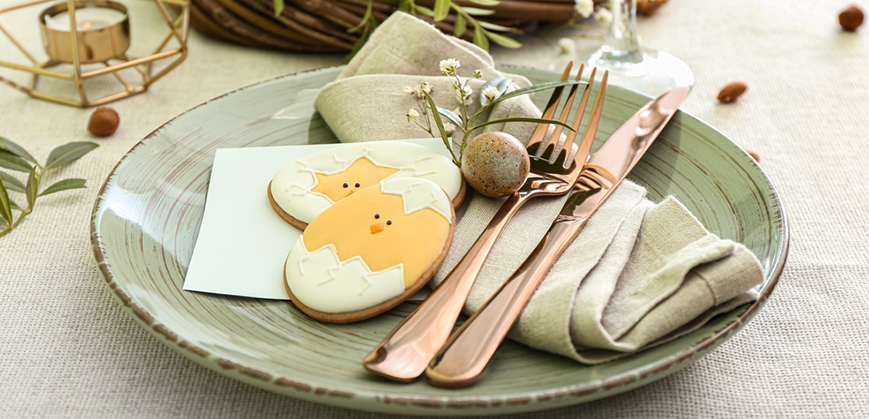 Décoration de table pour Pâques avec vaisselle verte pastel, couverts cuivre, et biscuits en forme de poussin