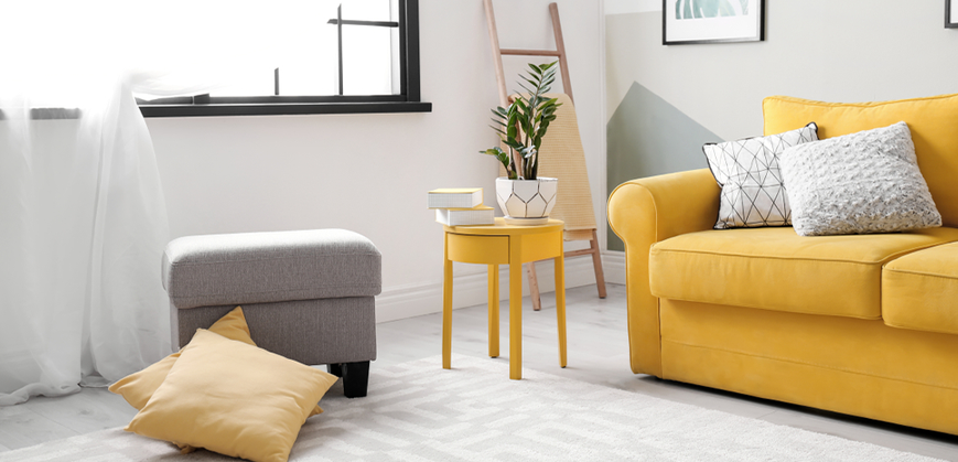 Séjour minimaliste lumineux avec canapé, petite table ronde et coussins jaunes 