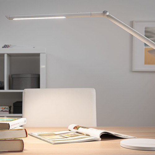 Lampe de bureau blanche au style moderne éclairant une revue posée sur une table en bois massif