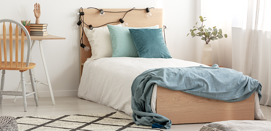 Lit simple en bois clair avec parure de lit blanche et oreillers bleus