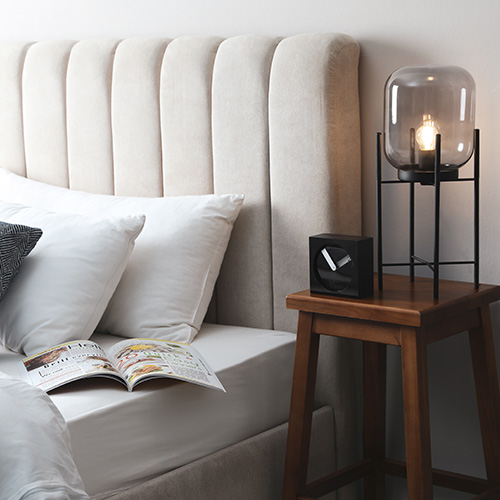 Lampe de chevet transparente sur une table de nuit en bois massif à côté d'un lit beige